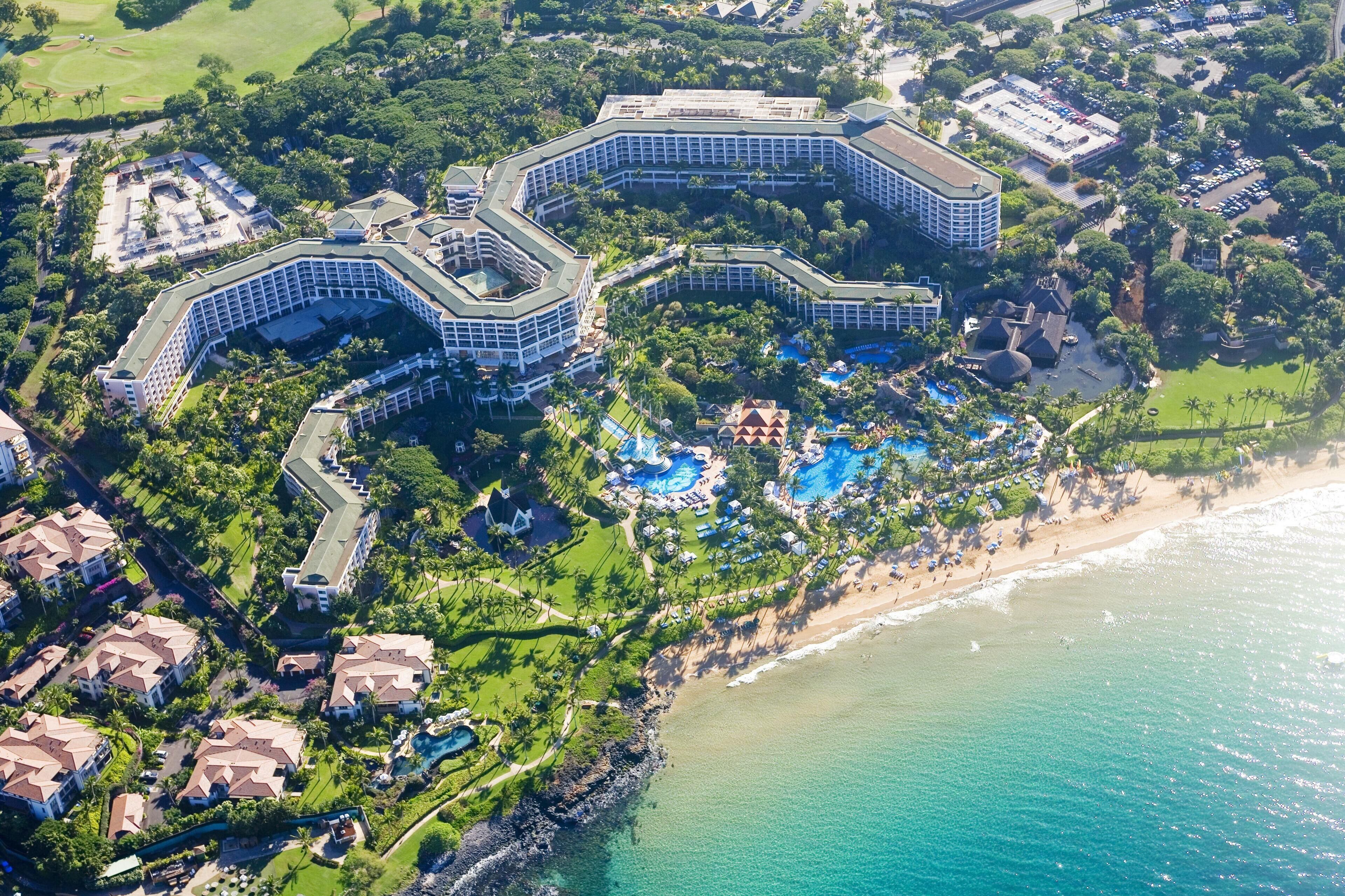 An aerial view of a resort with multiple buildings, a beach, and a pool area.
