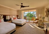 A hotel room with two beds, a ceiling fan, a dining table, and a view of palm trees.