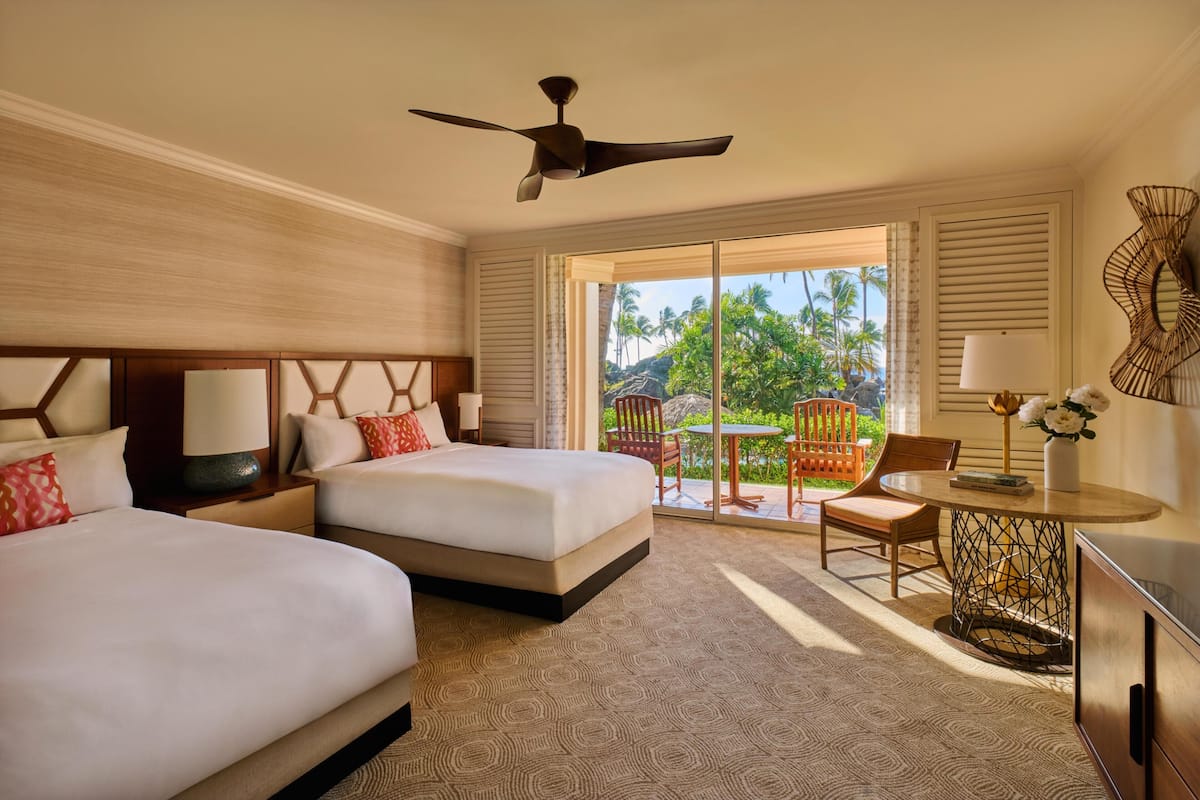 A hotel room with two beds, a ceiling fan, a dining table, and a view of palm trees.