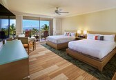 A hotel room with two beds, a desk, a chair, a TV, and a balcony with a view.