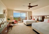 A hotel room with a balcony, two beds, a desk, and a chair.