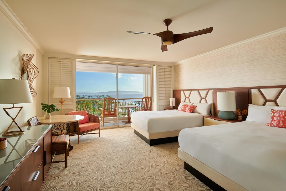 A hotel room with a balcony, two beds, a desk, and a chair.