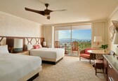 A hotel room with two beds, a balcony with a view, a ceiling fan, and a small dining area.