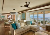 A spacious living area with a large sectional sofa, a chandelier, ceiling fans, and a balcony with a view.