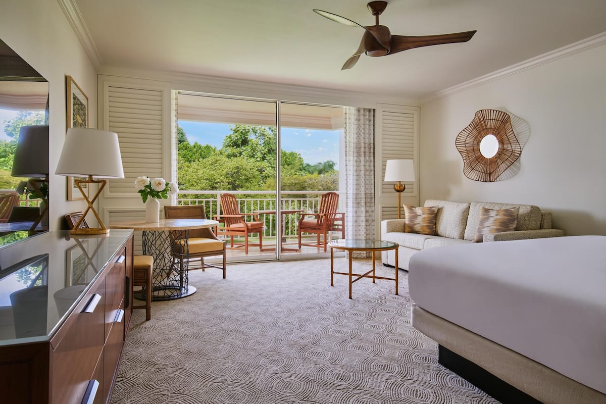A hotel room with a bed, a desk with a lamp, a chair, a table, and a balcony with chairs.