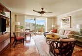A living room with a sofa, chairs, a coffee table, a TV, and a balcony with a view.