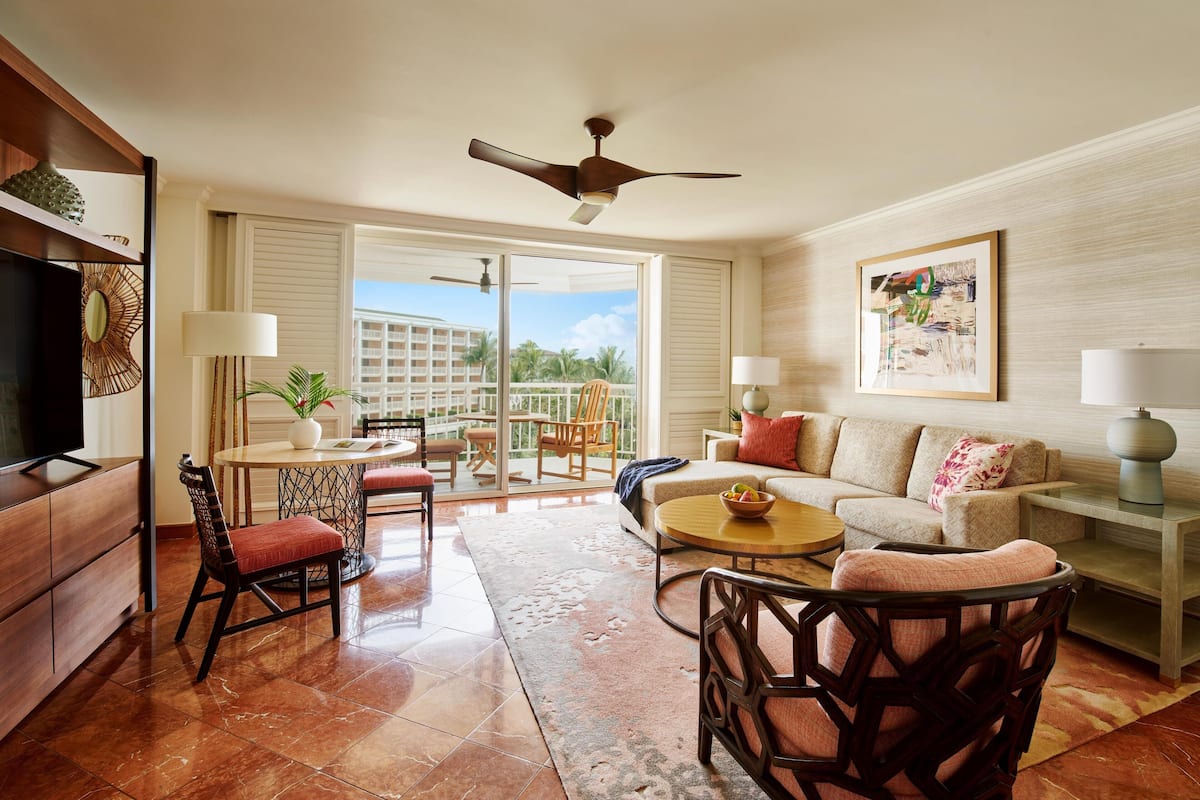 A living room with a sofa, chairs, a coffee table, a TV, and a balcony with a view.