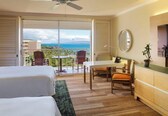 A hotel room with a bed, a desk, a chair, and a view of the ocean through a sliding door.