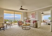 A spacious living area with a balcony, ceiling fans, a sofa, a coffee table, and a view of the ocean.