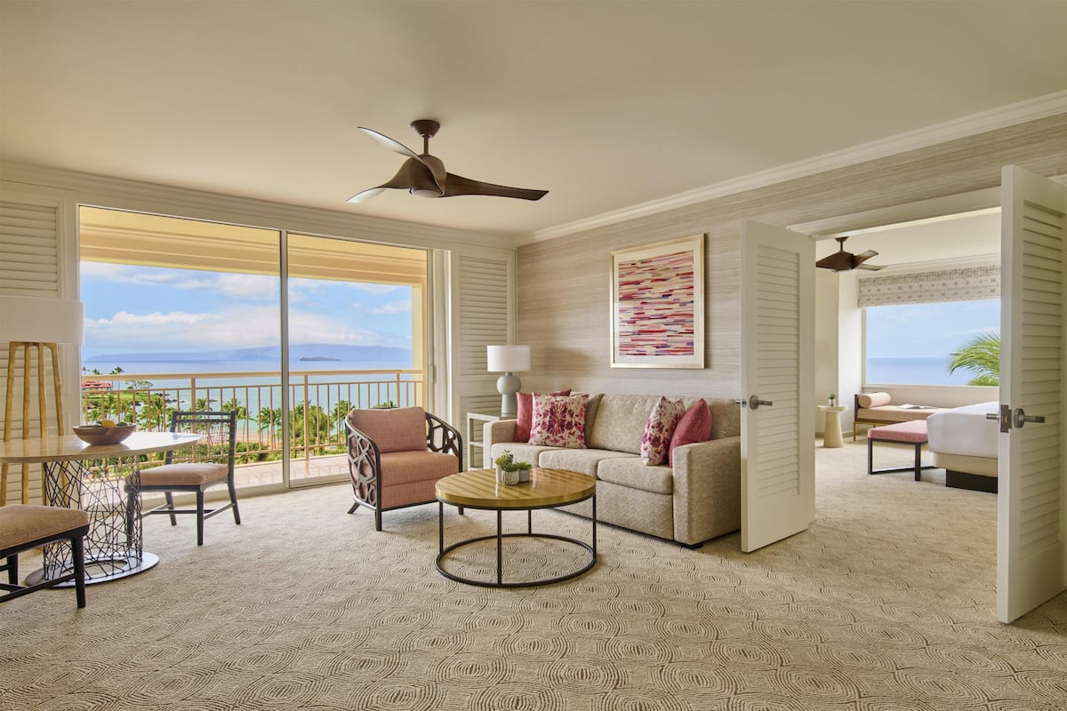 A spacious living area with a balcony, ceiling fans, a sofa, a coffee table, and a view of the ocean.
