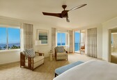 A spacious hotel room with a large bed, two chairs, a small table, and a ceiling fan.