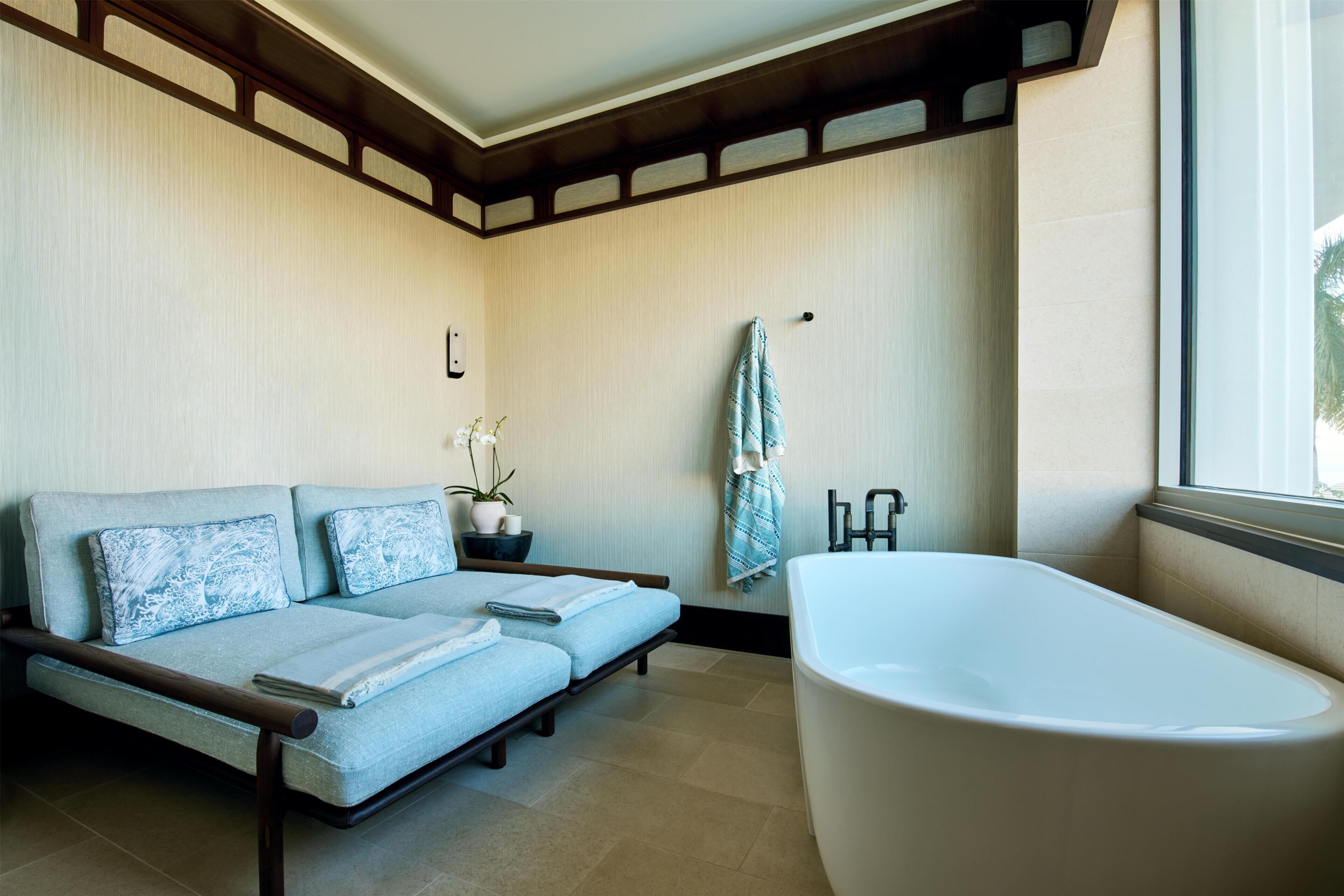 A modern bathroom with a bathtub, a sofa bed, and a potted plant.