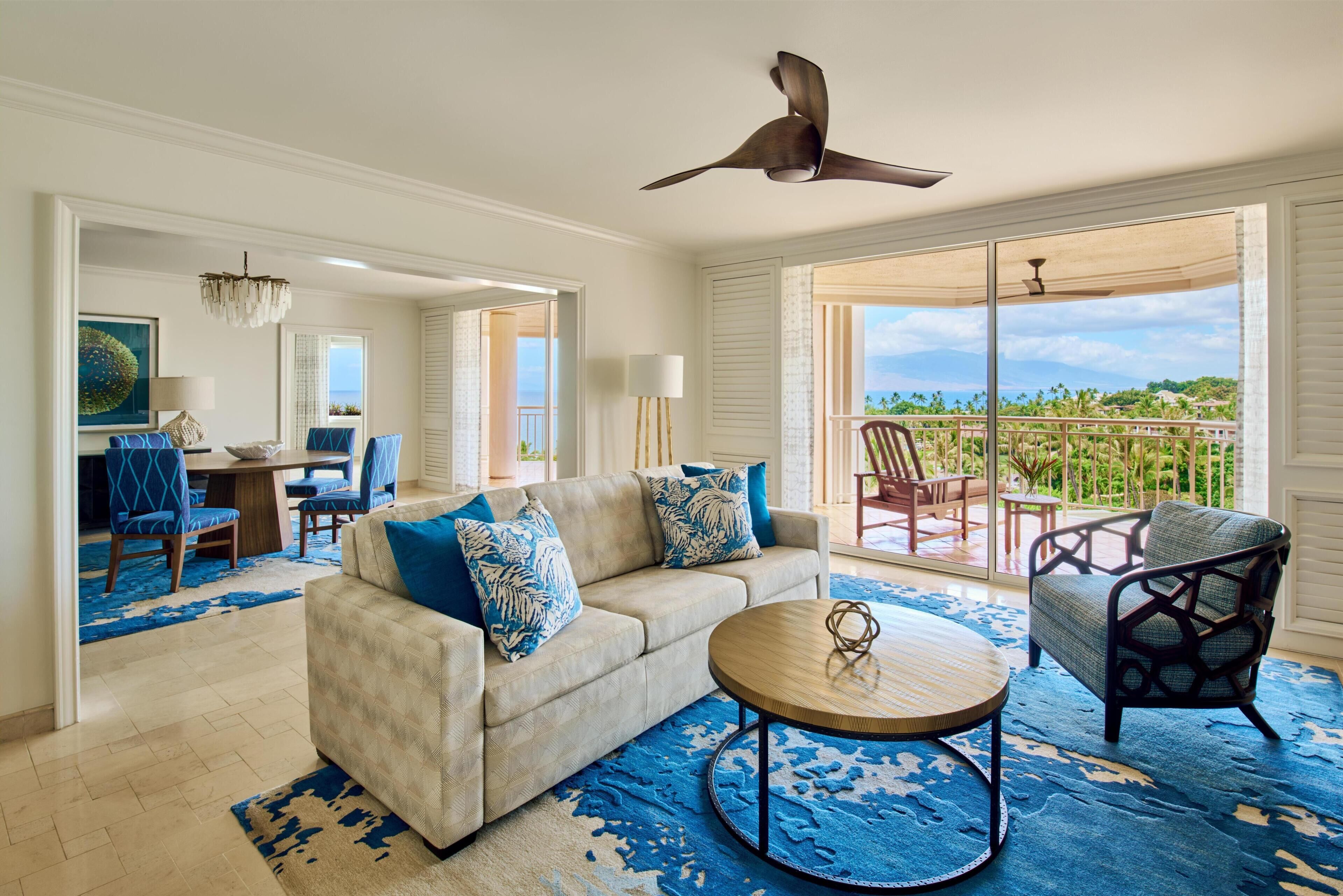 A living room with a sofa, coffee table, and chairs, a dining area with a table and chairs, and a balcony with a view.