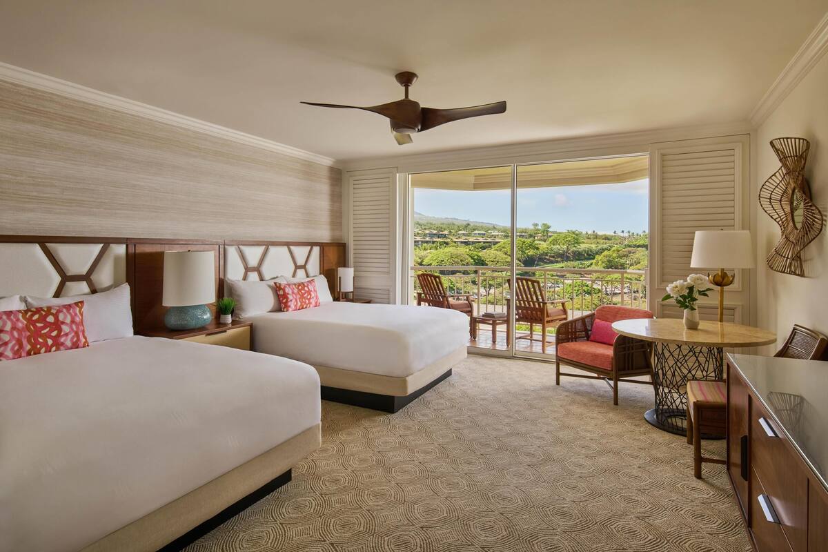 A hotel room with two beds, a ceiling fan, a balcony with a view, and a dining area.