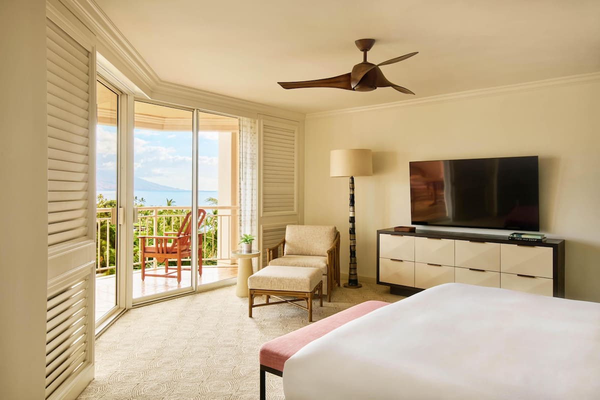 A hotel room with a bed, a television, a chair, a desk, and a balcony with a view.