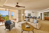 A living room with a sofa, armchair, and coffee table, a dining area with chairs, and a view of the ocean.