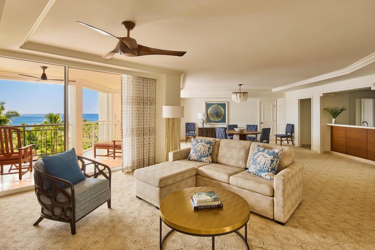 A living room with a sofa, armchair, and coffee table, a dining area with chairs, and a view of the ocean.