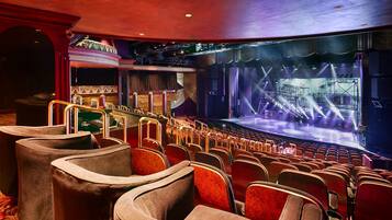 Une salle de spectacle dotée de rangées de sièges rouges moelleux, d’une scène éclairée et d’un décor.