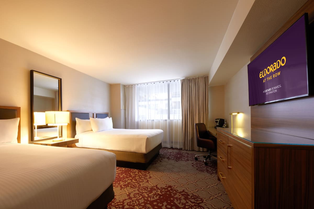 A hotel room with two beds, a desk, a chair, a TV, and a window with curtains.