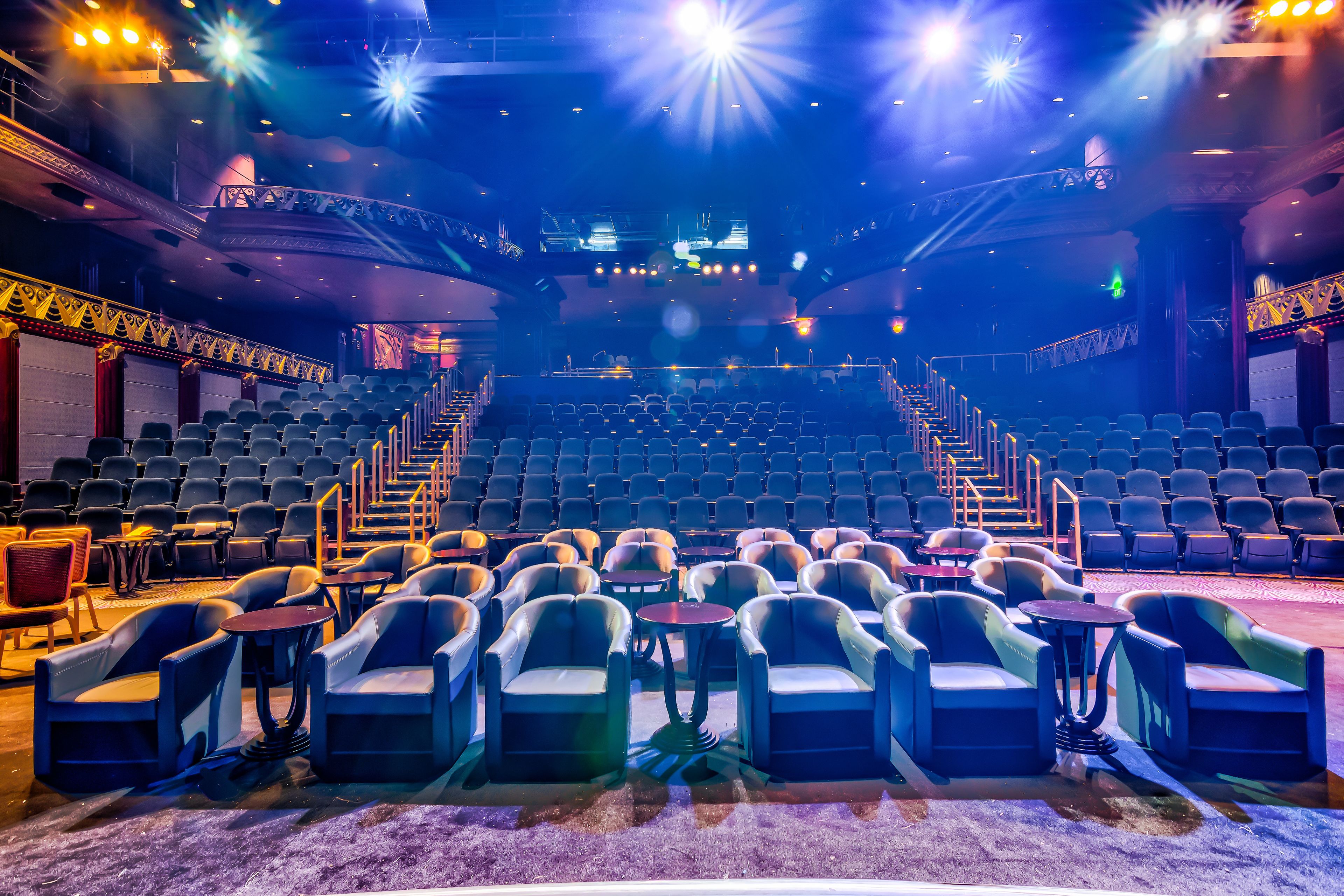 An indoor theater with rows of seats, a stage, and a staircase leading to the upper level.