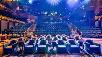 An indoor theater with rows of seats, a stage, and a staircase leading to the upper level.