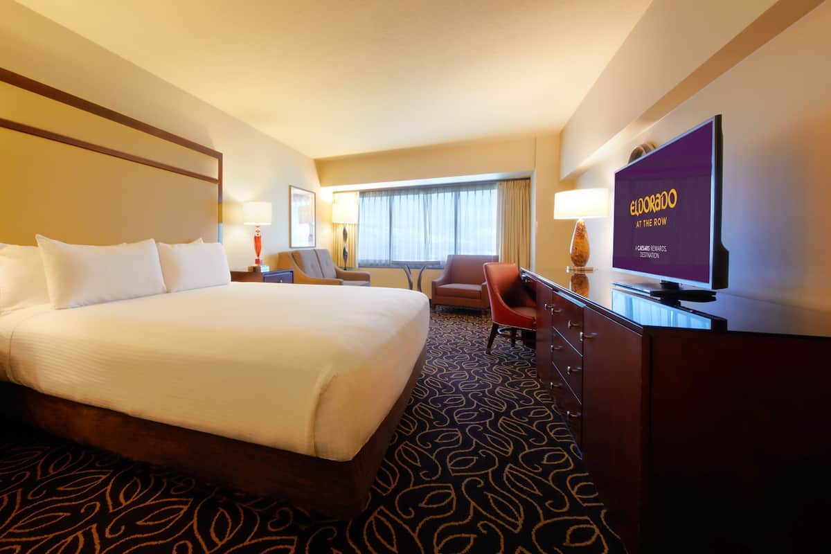 A hotel room with a large bed, a desk, a chair, a television, and a window with curtains.