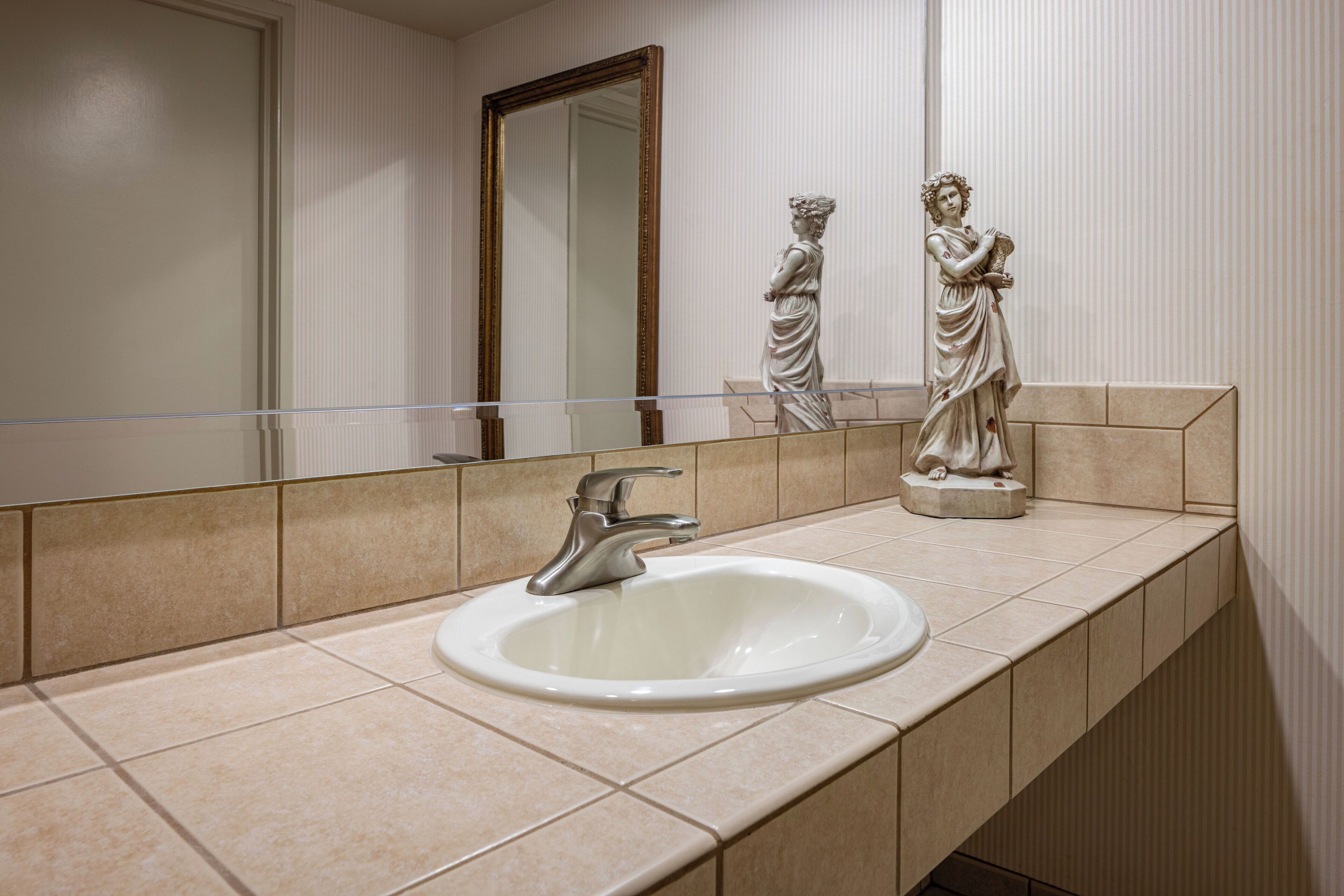 A bathroom with a white sink, a mirror, and a statue on the counter.