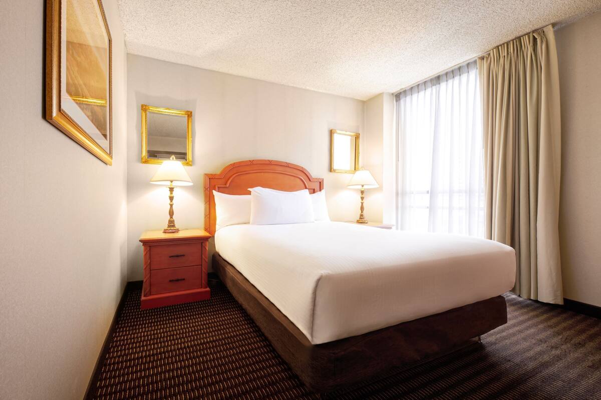 A hotel room with a large bed, two bedside tables with lamps, a mirror, and a window with curtains.