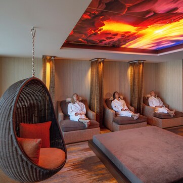 A modern spa room with three massage chairs, a hanging chair, and a massage table.