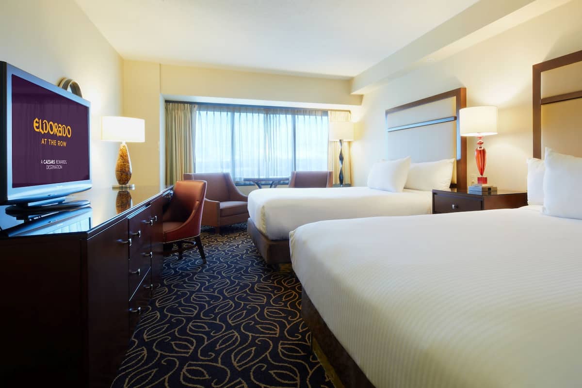 A hotel room with two beds, a desk with a television, and a seating area with chairs.