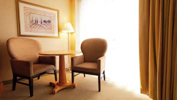 A hotel room with two armchairs, a small round table, a lamp, and a framed picture on the wall.