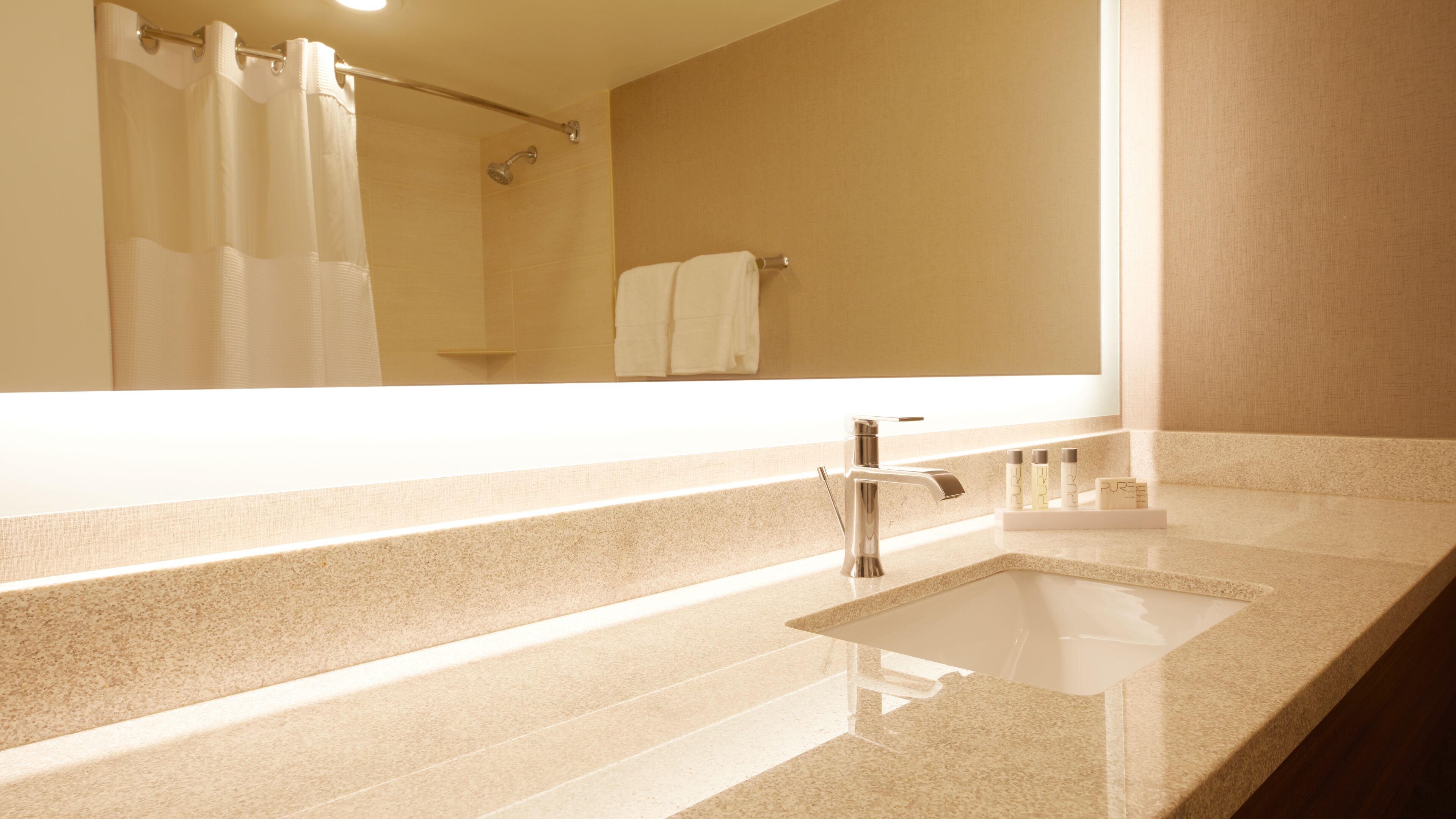 A bathroom with a large mirror, a sink, and a shower area.