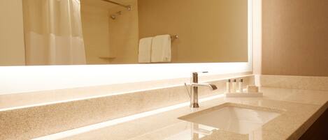 A bathroom with a large mirror, a sink, and a shower area.