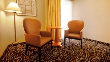 A hotel room with two armchairs, a small round table, a floor lamp, and a patterned carpet.