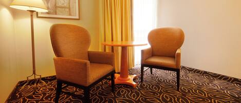 A hotel room with two armchairs, a small round table, a floor lamp, and a patterned carpet.
