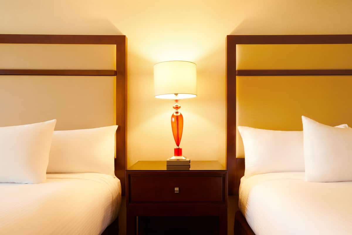 A hotel room with two beds, a nightstand with a lamp, and a wooden headboard.