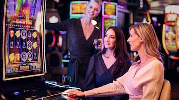 A slot machine with various symbols and a display screen, a person interacting with the machine, and another person standing in the background.