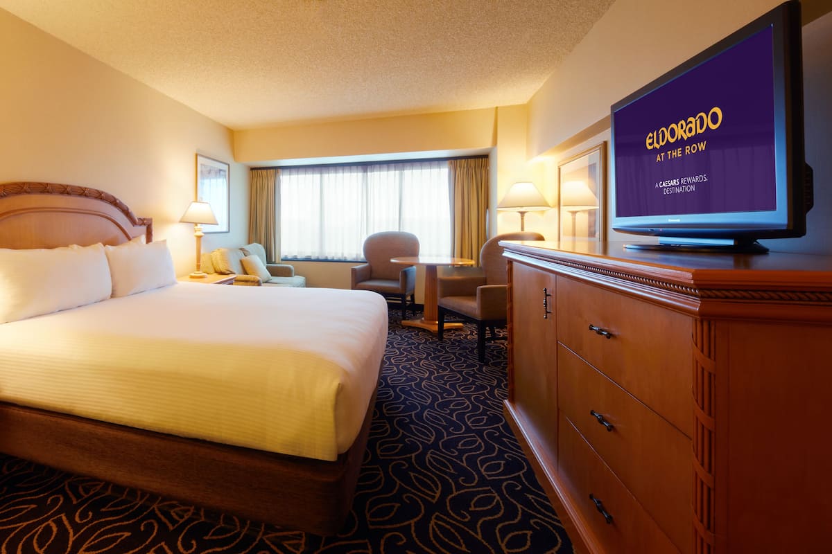A hotel room with a large bed, a desk, a chair, a television, and a wardrobe.