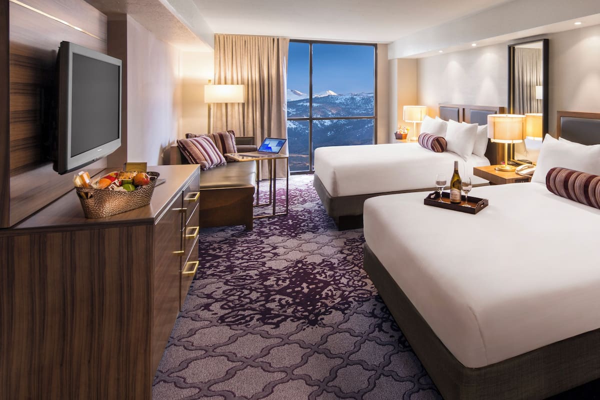 A hotel room with two beds, a TV, a desk with a laptop, and a view of a snowy mountain.