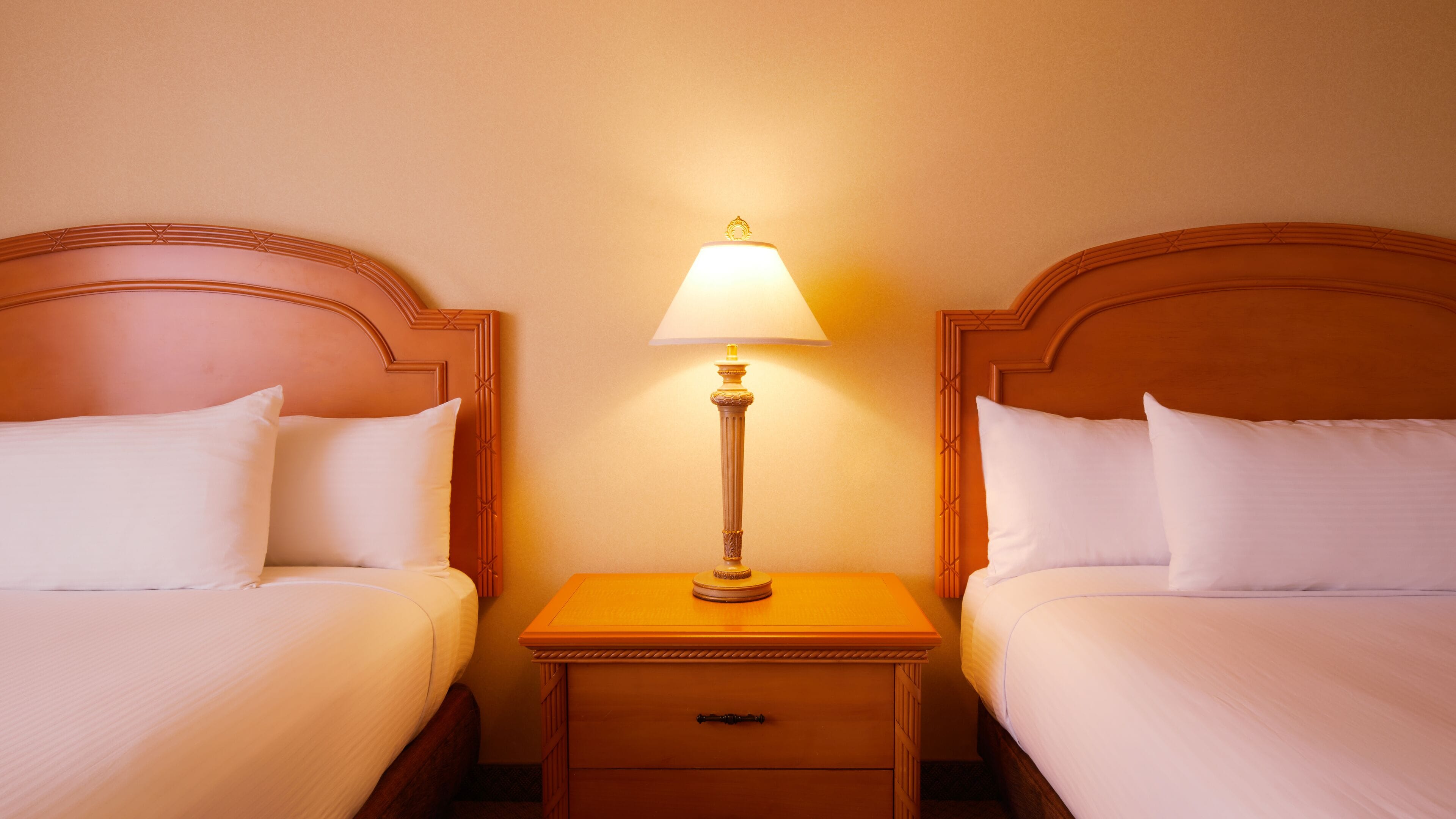 Een hotelkamer met twee bedden, een nachtkastje met een lamp en een klein lade.