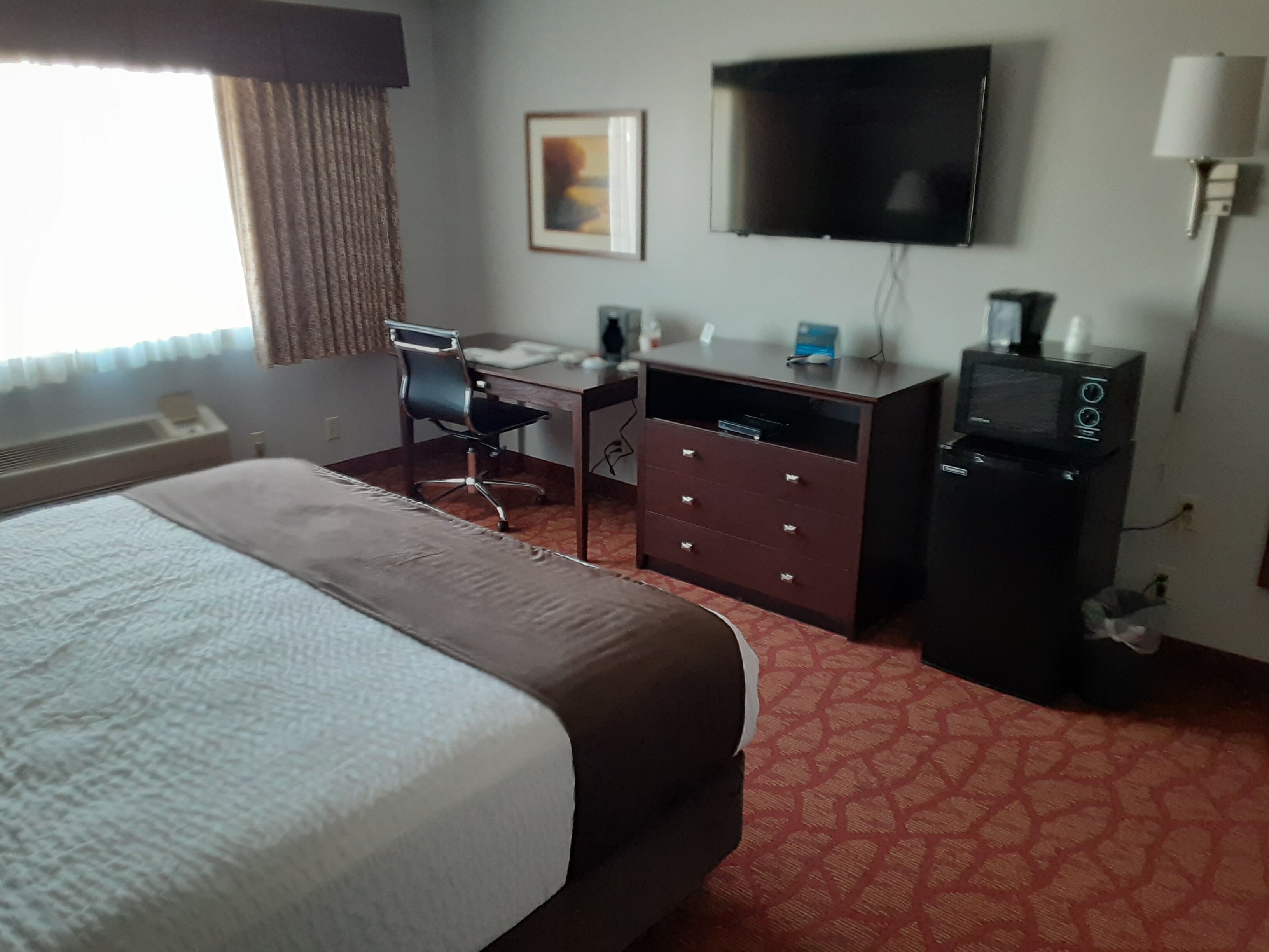 Een hotelkamer met een bed, een bureau, een televisie en een dressoir.