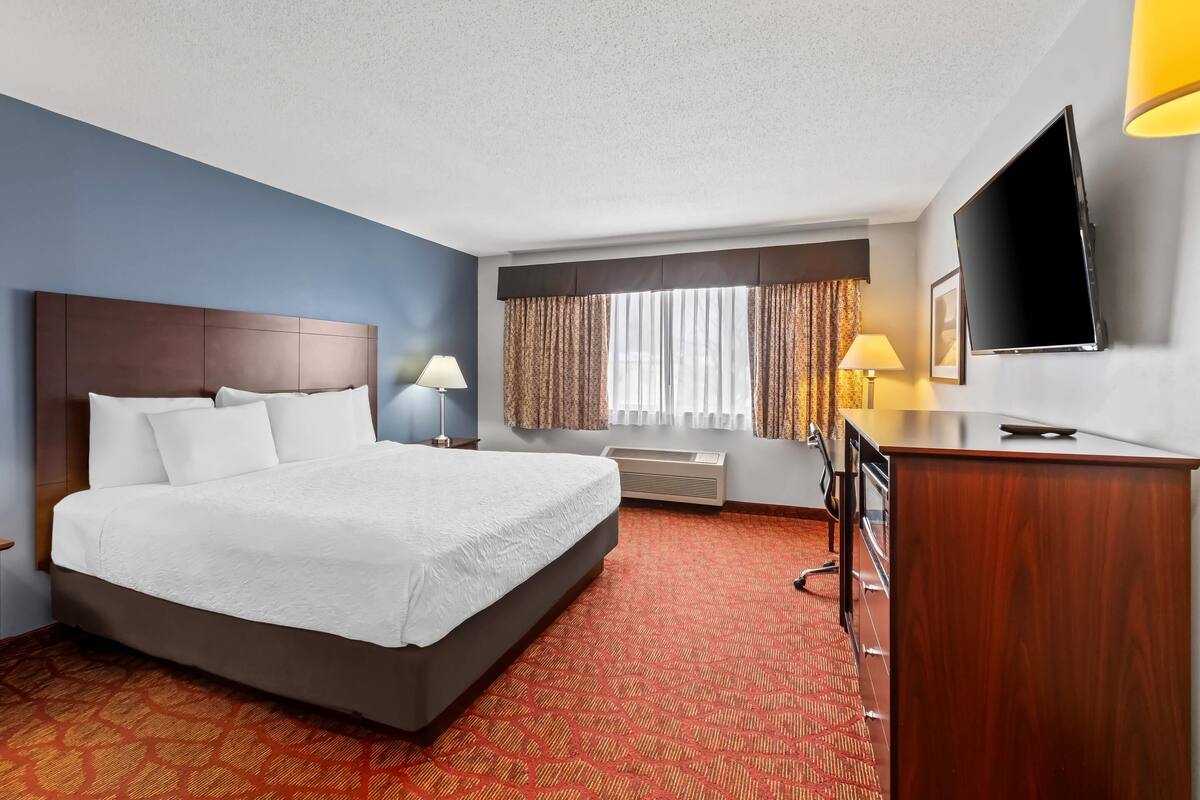 A hotel room with a large bed, a desk, a flat-screen TV, and a window with curtains.