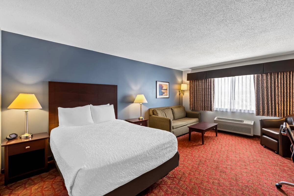 A hotel room with a large bed, two bedside tables with lamps, a sofa, a desk, and a chair.