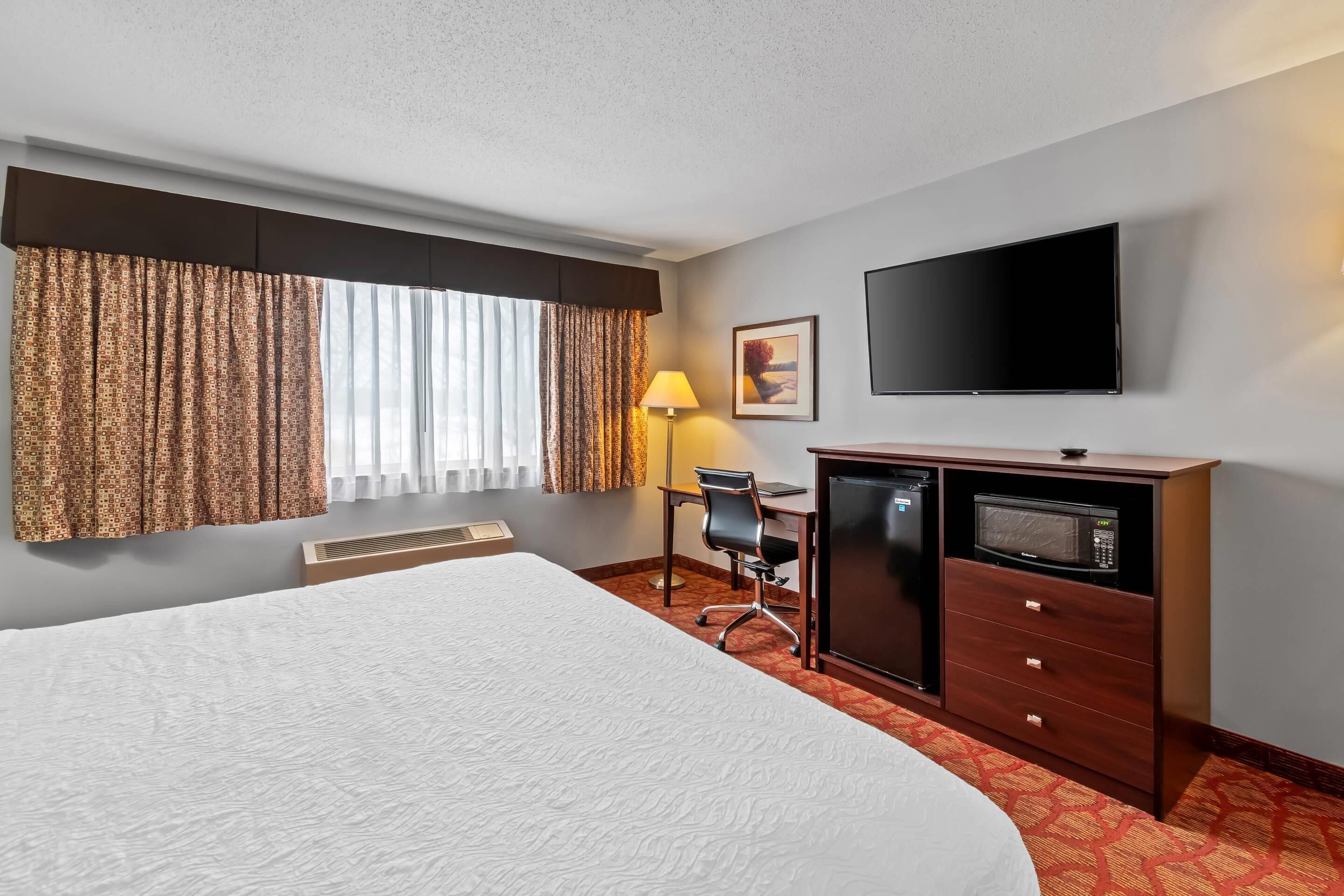 Hotelkamer met een groot bed, een bureau met stoel, een flatscreen televisie, een magnetron en een raam met gordijnen.