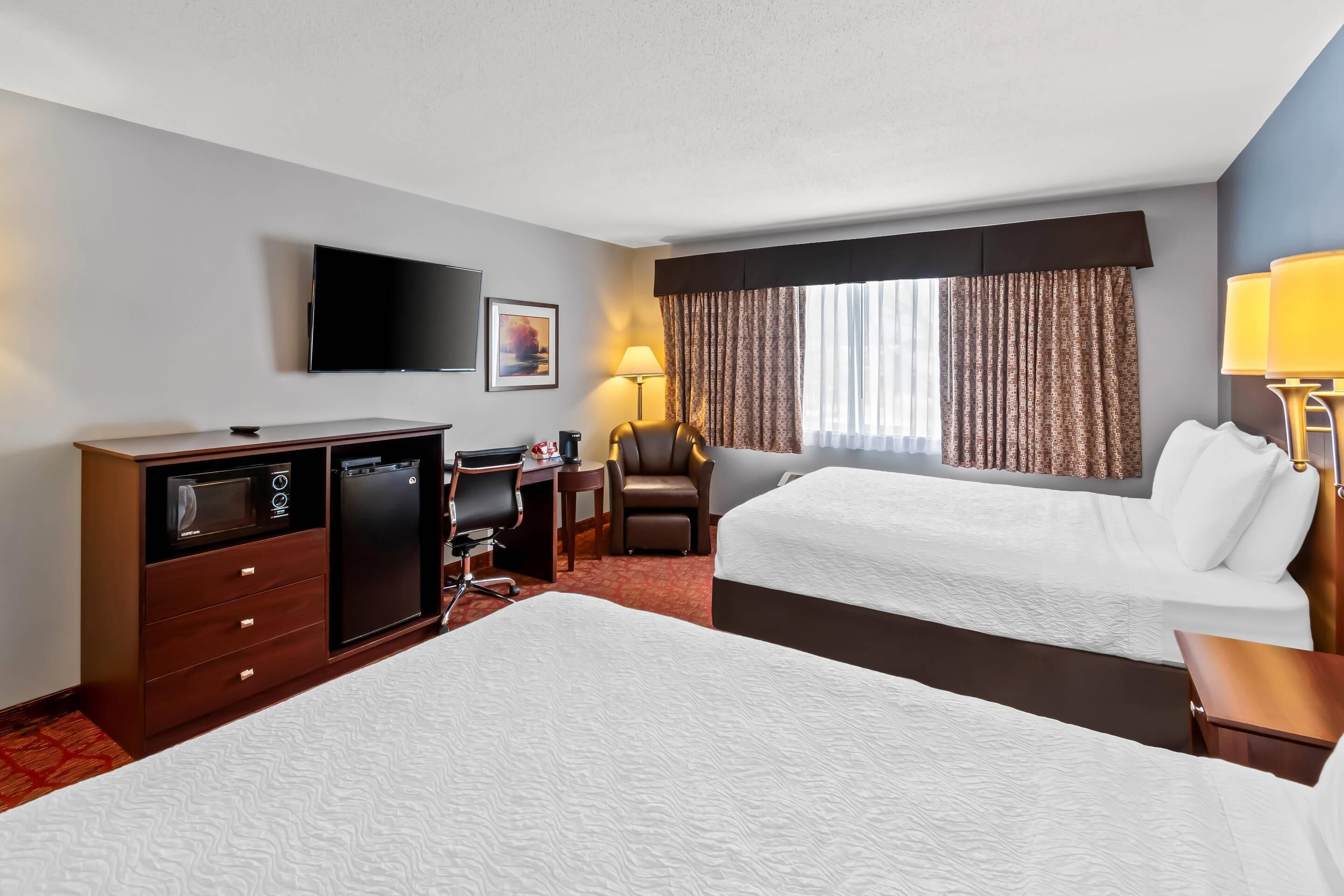 A hotel room with two beds, a desk with a chair, a television, a lamp, and a minibar.