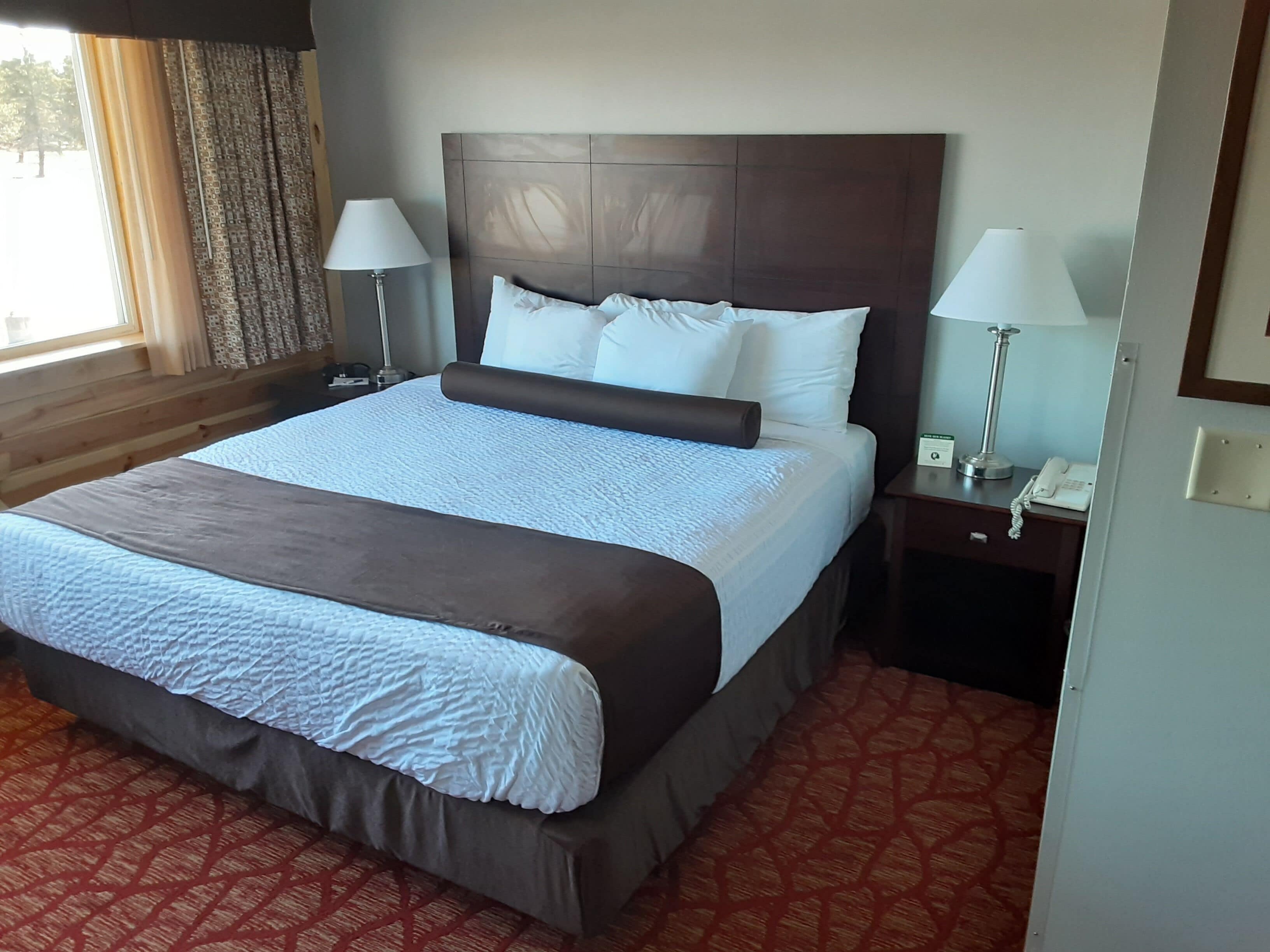 A hotel room with a large bed, two bedside tables, a telephone, and a window with curtains.