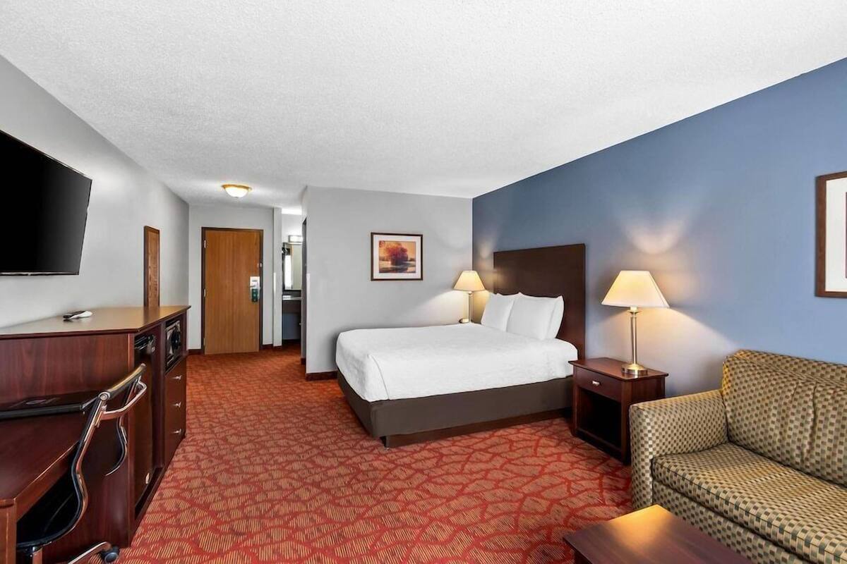 A hotel room with a bed, two bedside lamps, a TV, a desk, and a sofa.