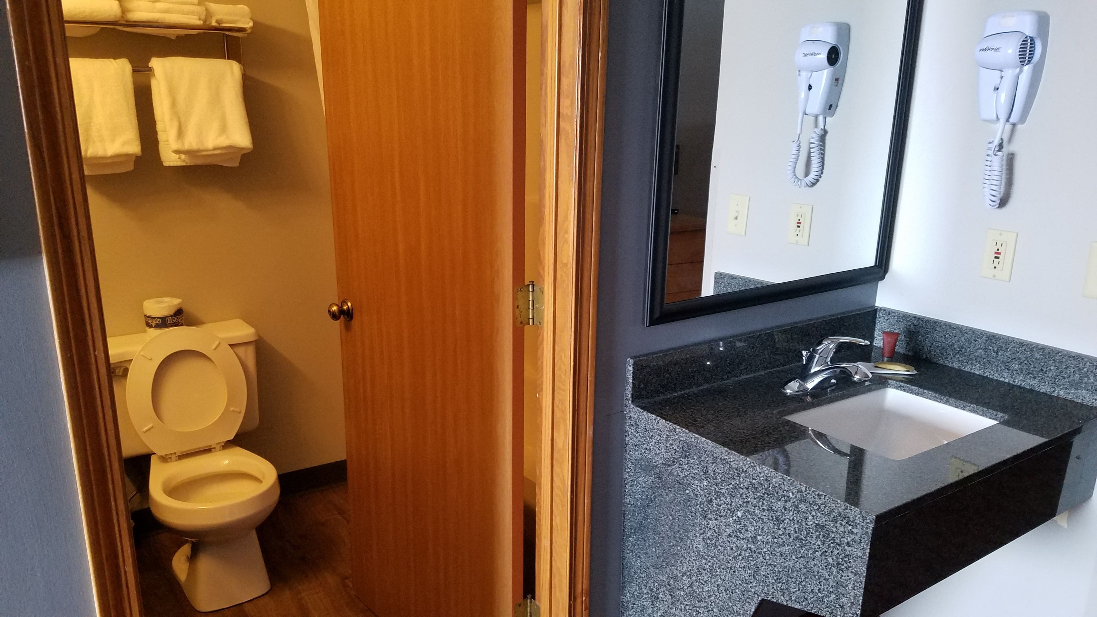 A bathroom with a toilet, a sink, and two hair dryers mounted on the wall.
