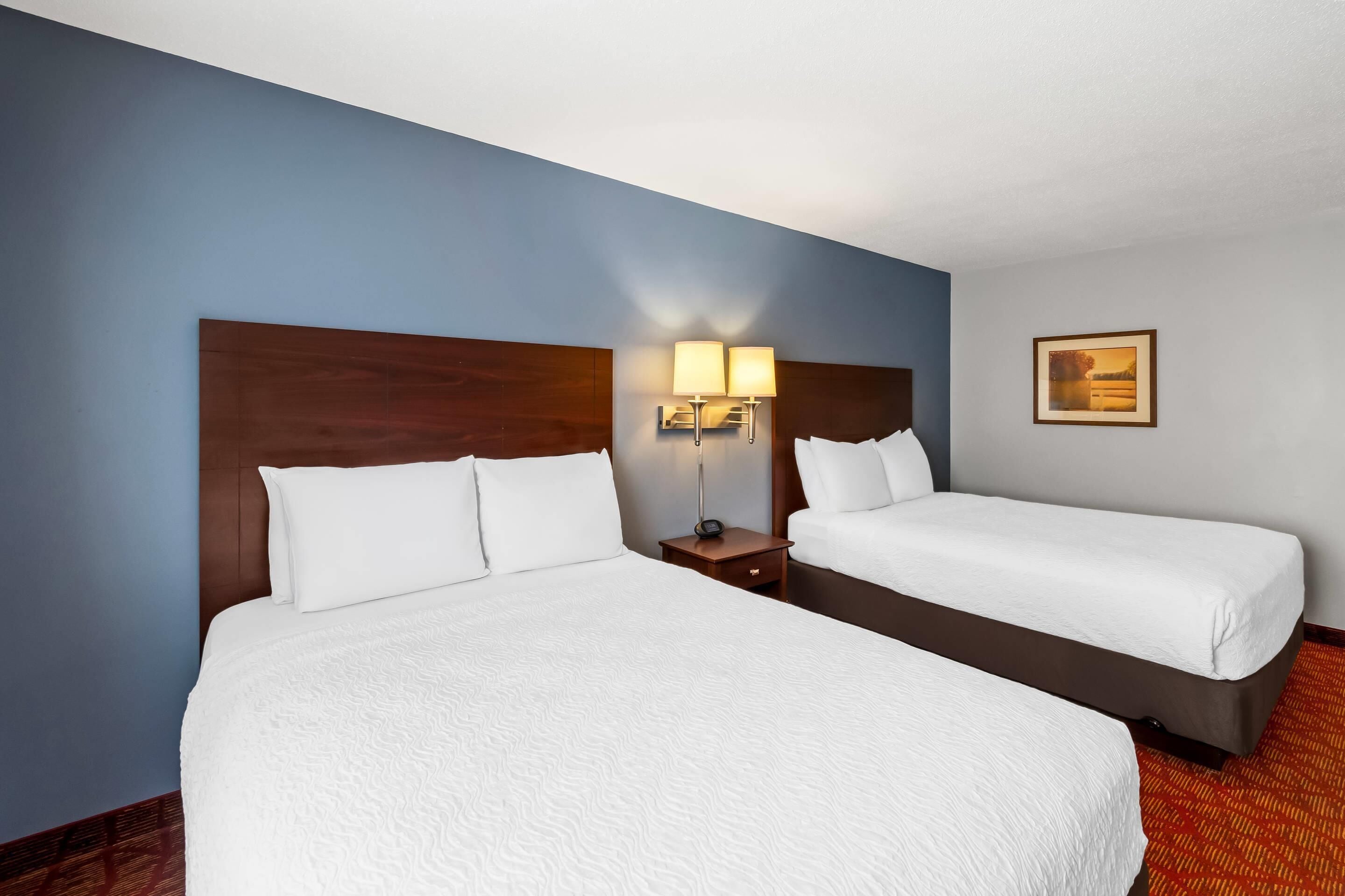 A hotel room with two beds, a nightstand with a lamp, and a framed picture on the wall.