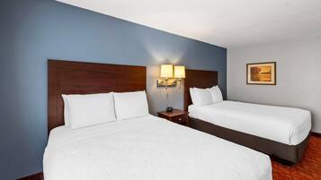 A hotel room with two beds, a nightstand with a lamp, and a framed picture on the wall.